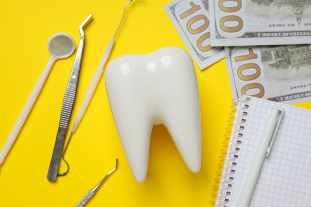 Dental tools, money, decorative tooth and notepad on yellow background, closeup