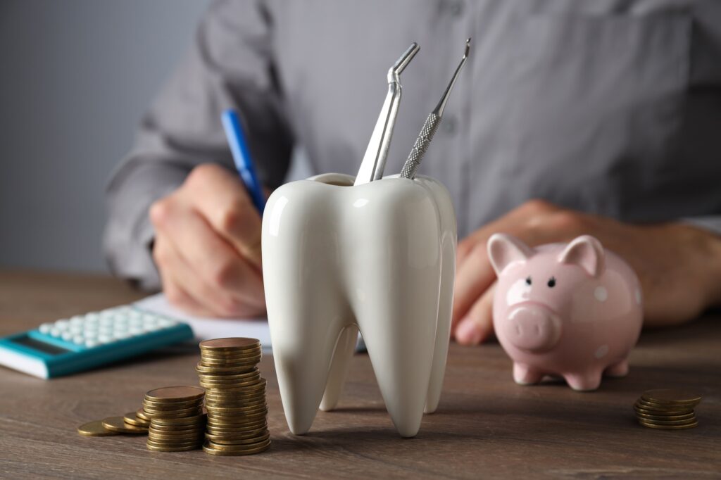 Tooth with dental instruments, piggy bank, calculator and coins on table on gray background