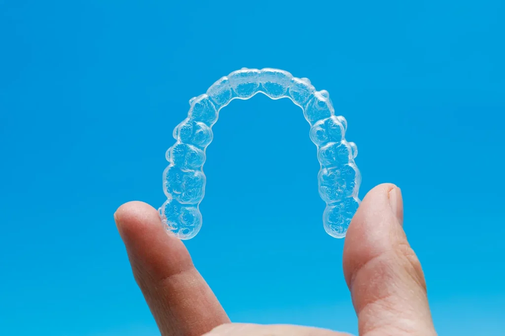 hand holding one transparent retainer on blue background invisalign orthodontics concept
