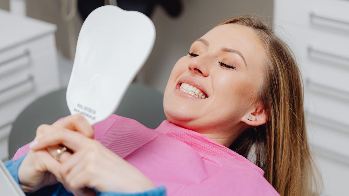 Patient checking their teeth with a hand mirror in a dental chair
