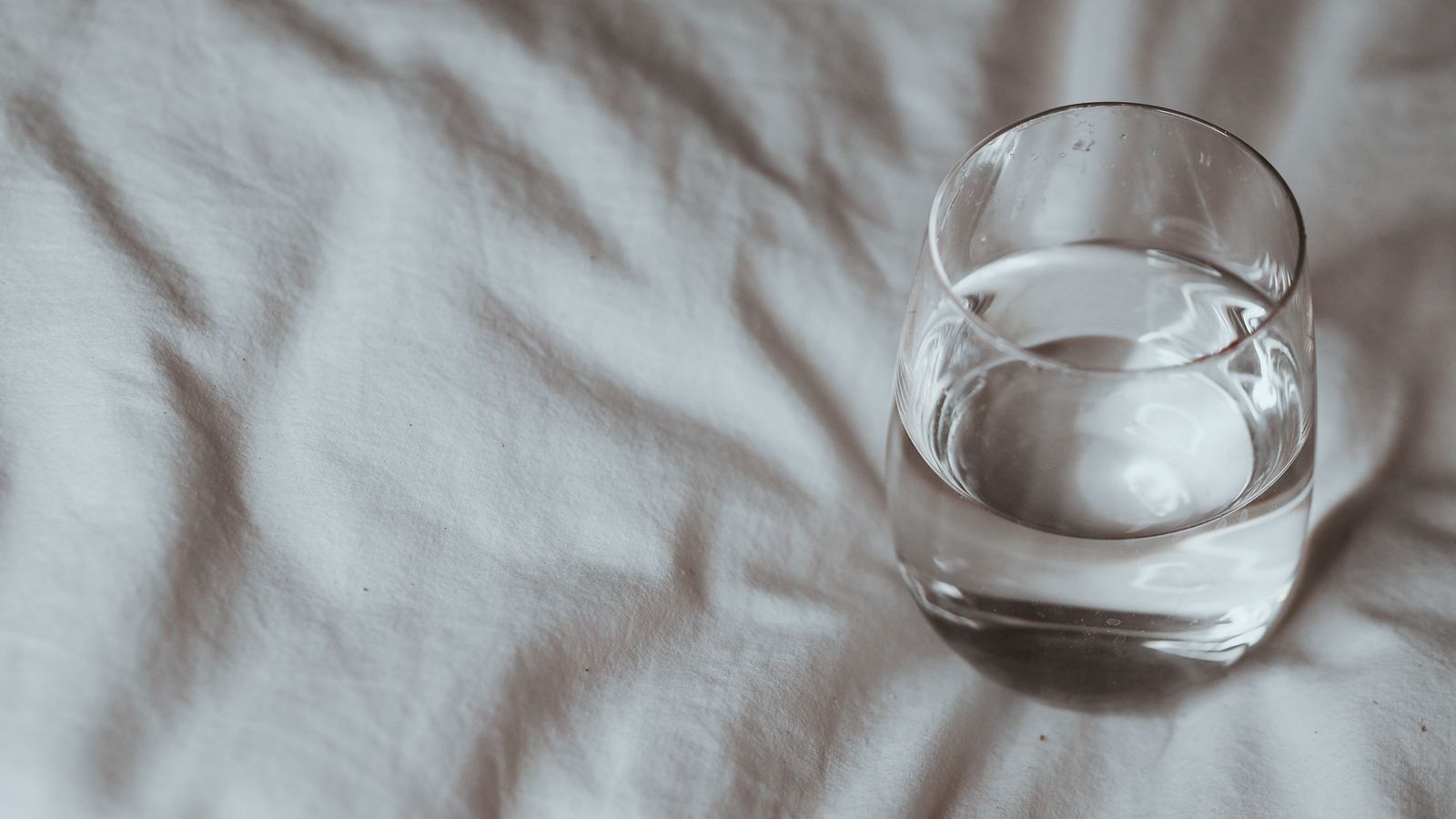 Glass of water on a white bedsheet in morning light