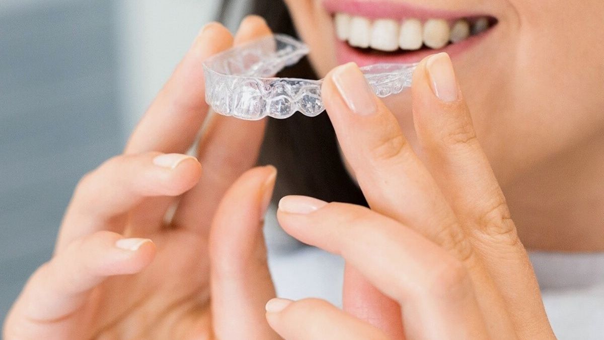 Hands holding a clear dental appliance up to a smile