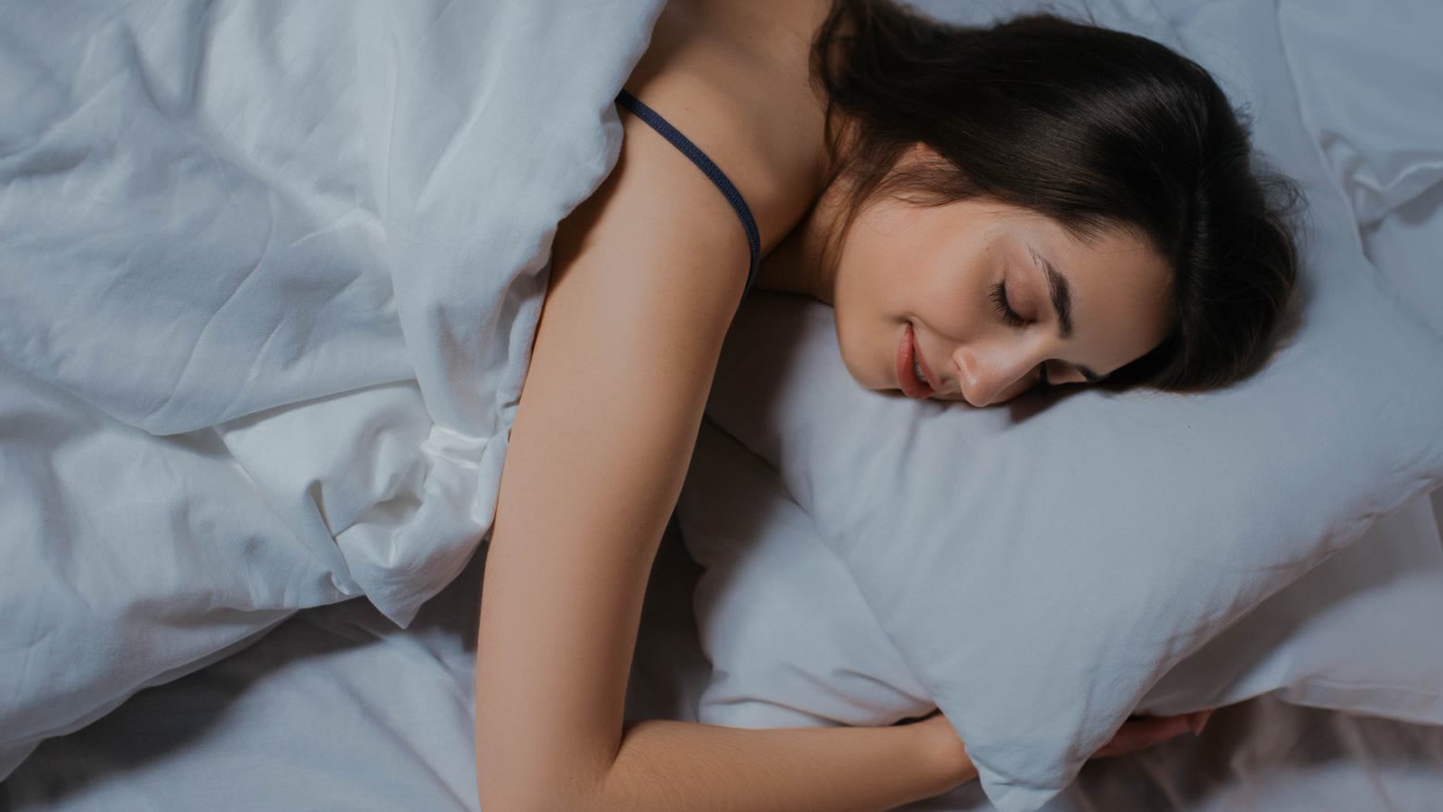 Woman sleeping peacefully on her side in a bed with pale blue linens