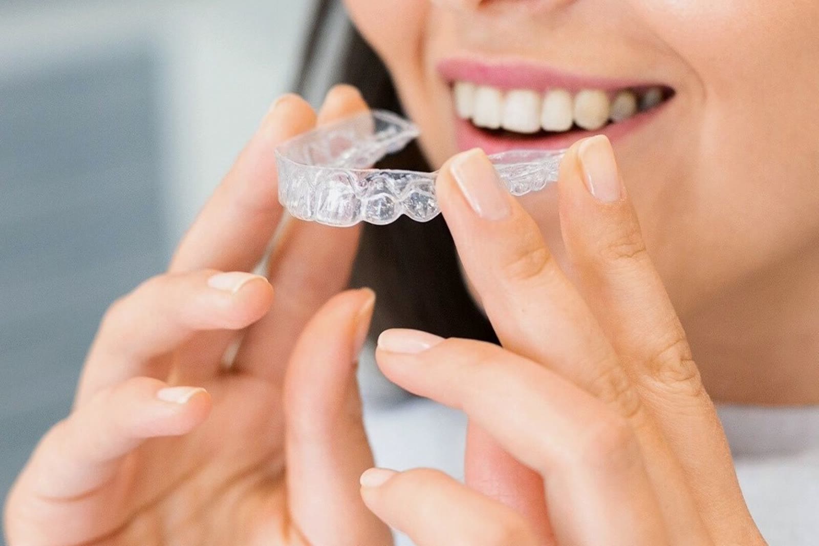 Smiling woman holding a clear dental aligner tray
