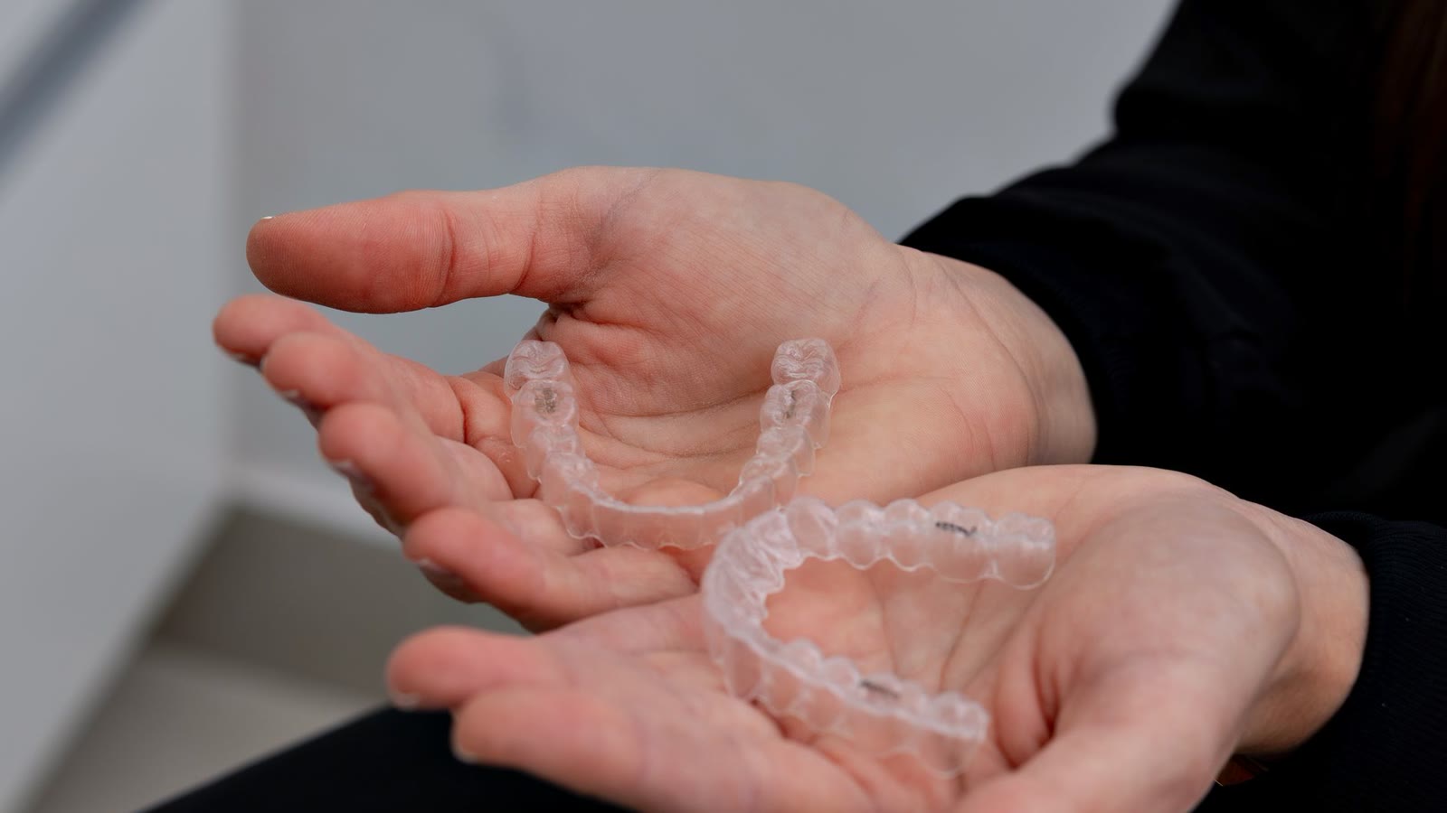 Two hands holding a pair of clear dental aligners