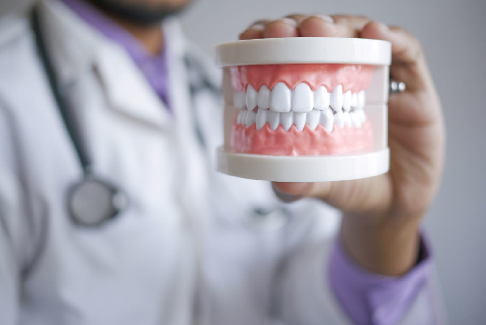 Hand holding a model of upper and lower teeth set in a pink denture base
