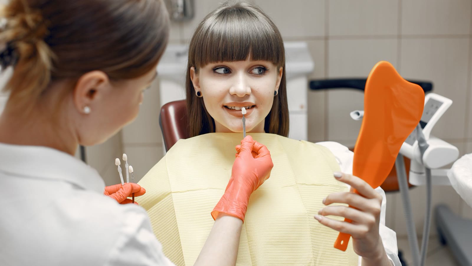 Dental professional showing a smiling patient her teeth in a hand mirror