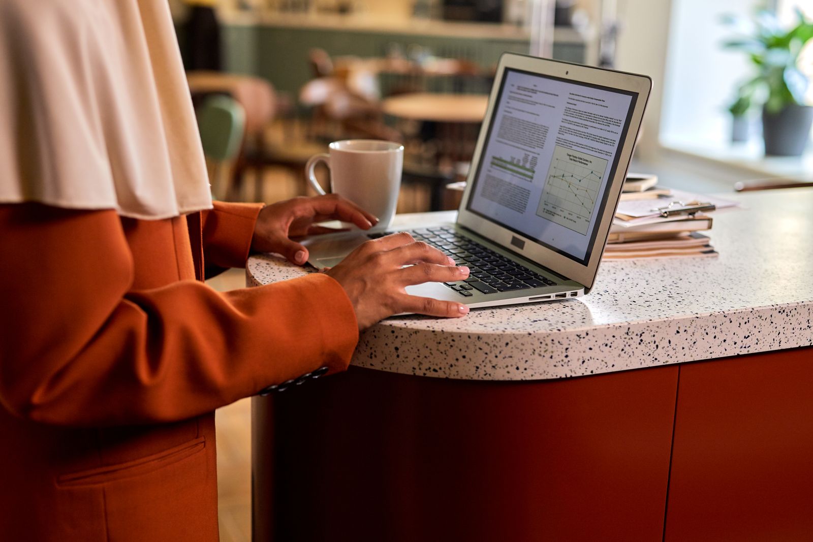 Adult woman typing on a laptop at a modern office counter, coffee beside her in a casual indoor setting
