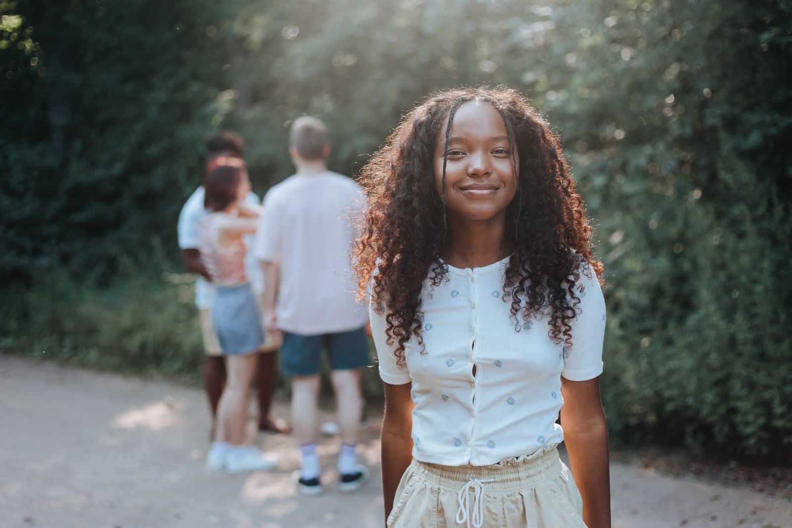 Teen girl smiling in a summer park, friends in background on a sunny day