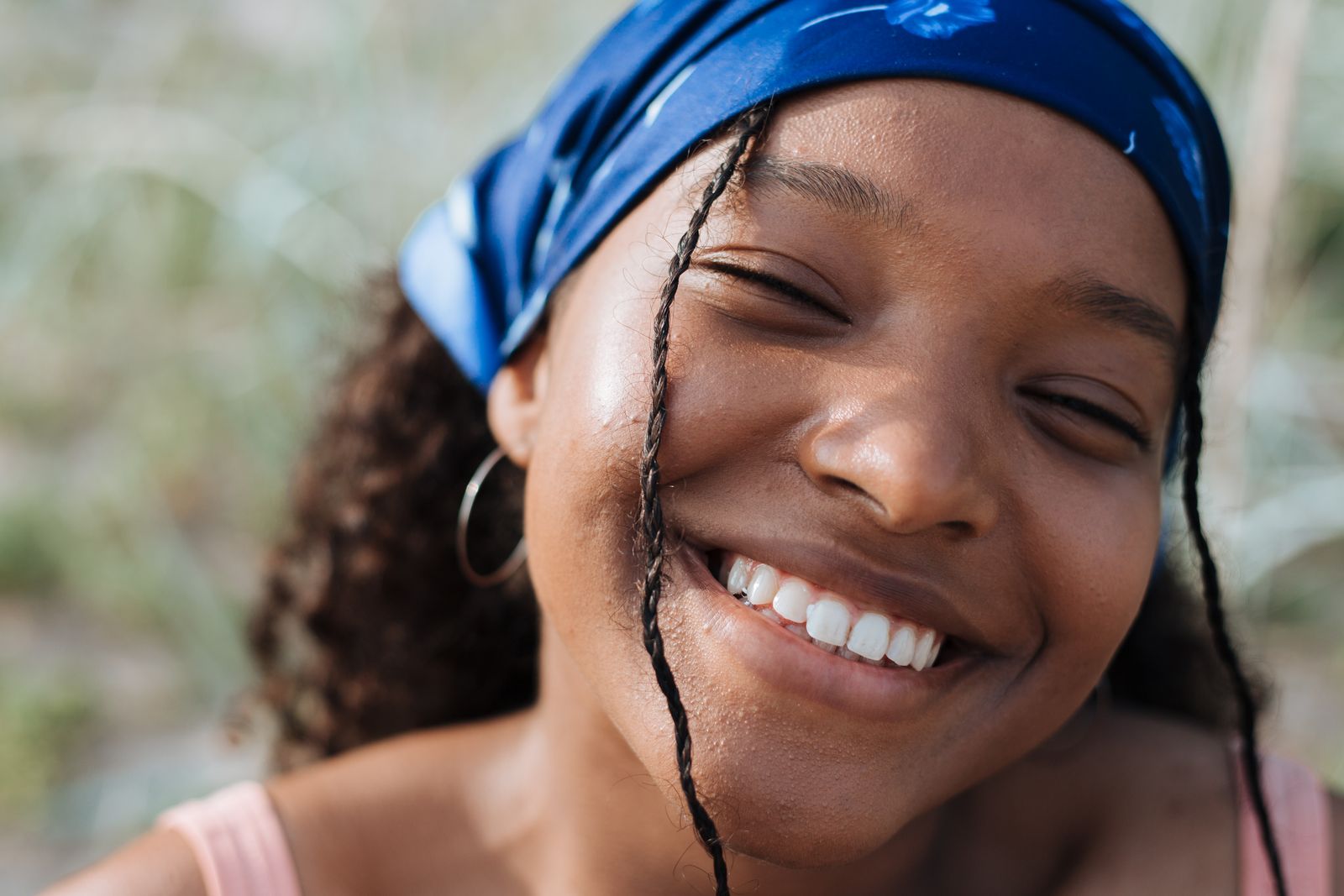 Close-up portrait of a smiling teenager wearing a blue bandana enjoying a sunny day outdoors