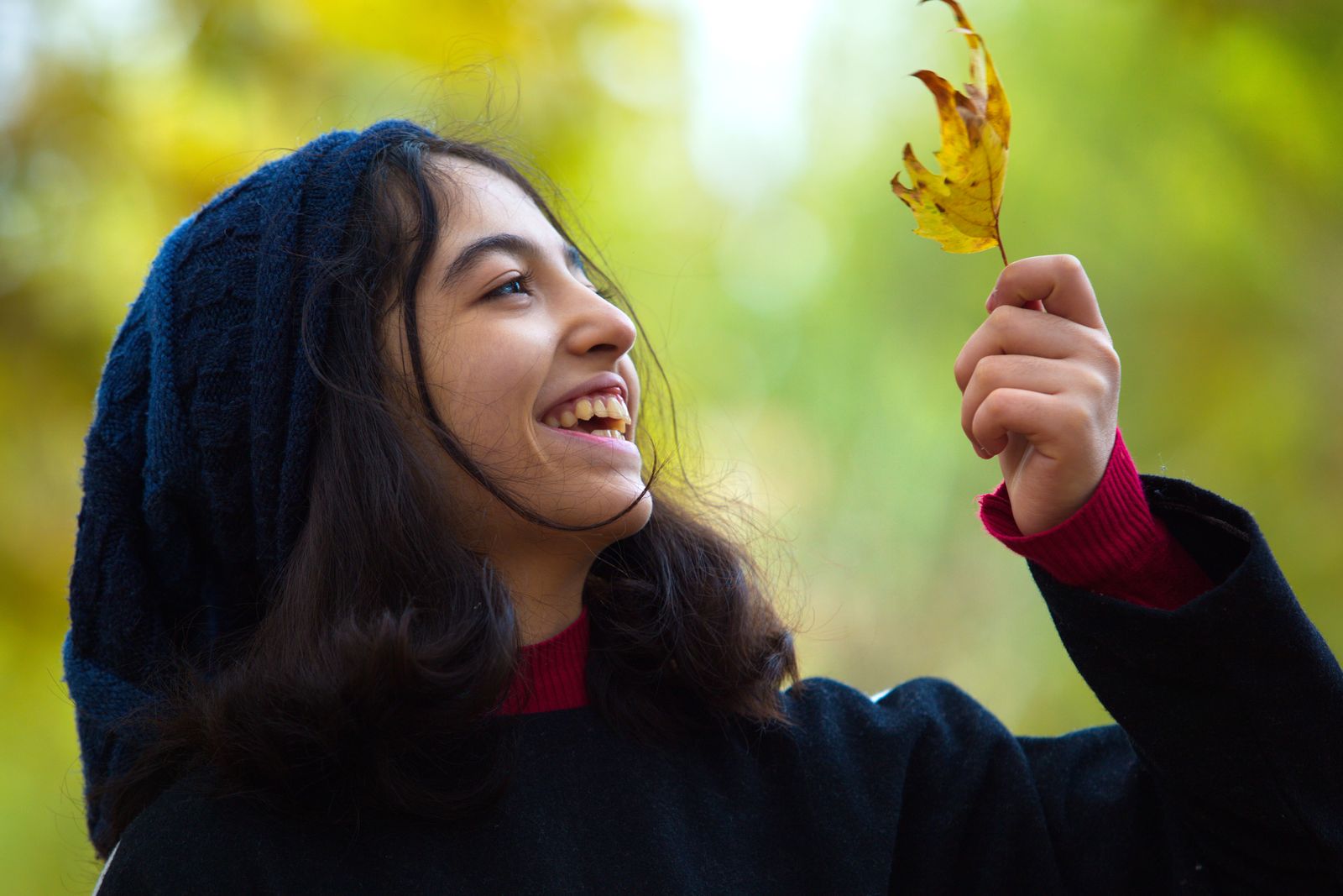 Happy teenage girl holding a fall leaf with a joyful expression, embodying the spirit of autumn