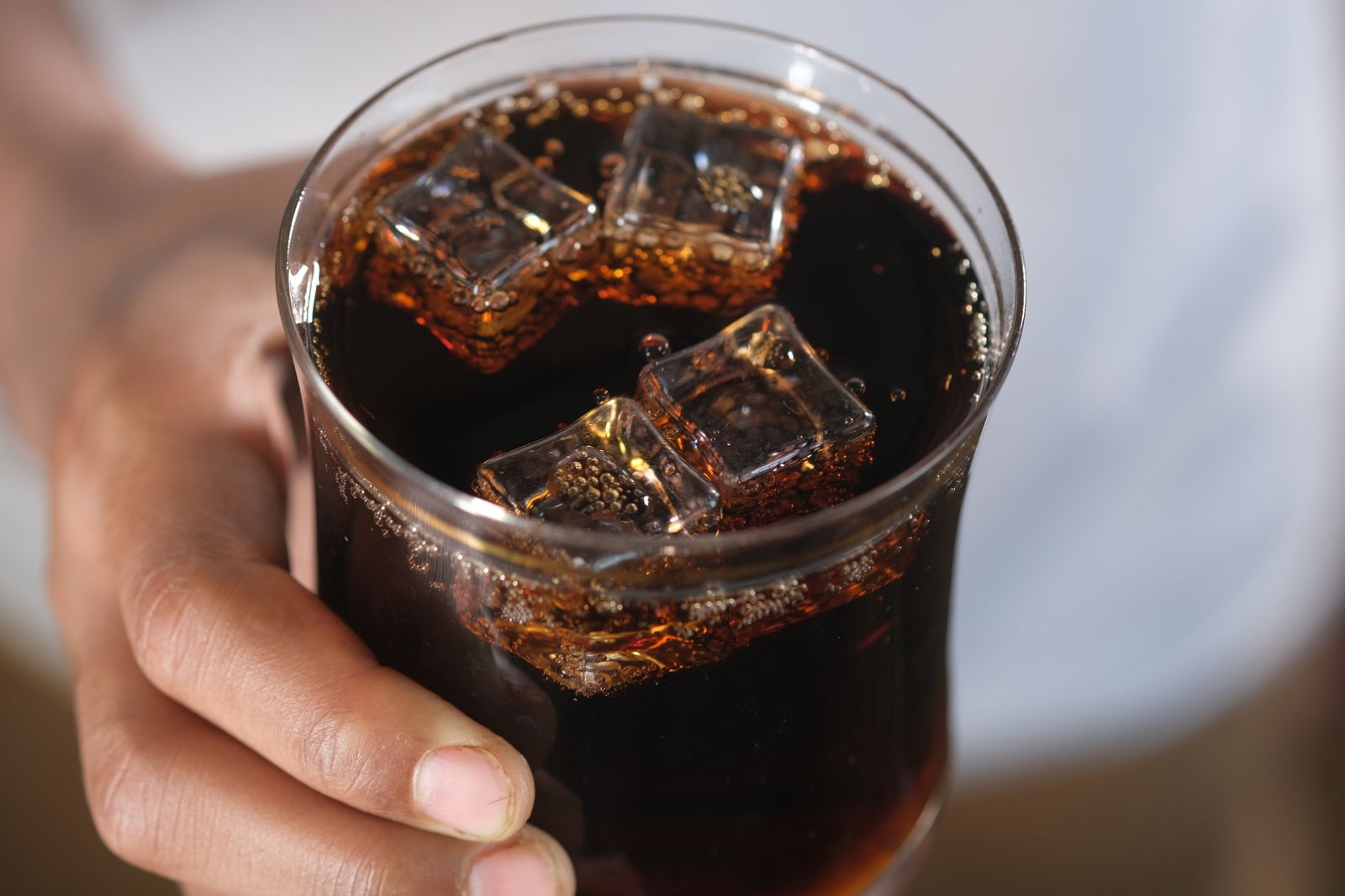 Close-up of a hand holding a glass of dark soda with ice cubes, creating a refreshing feel
