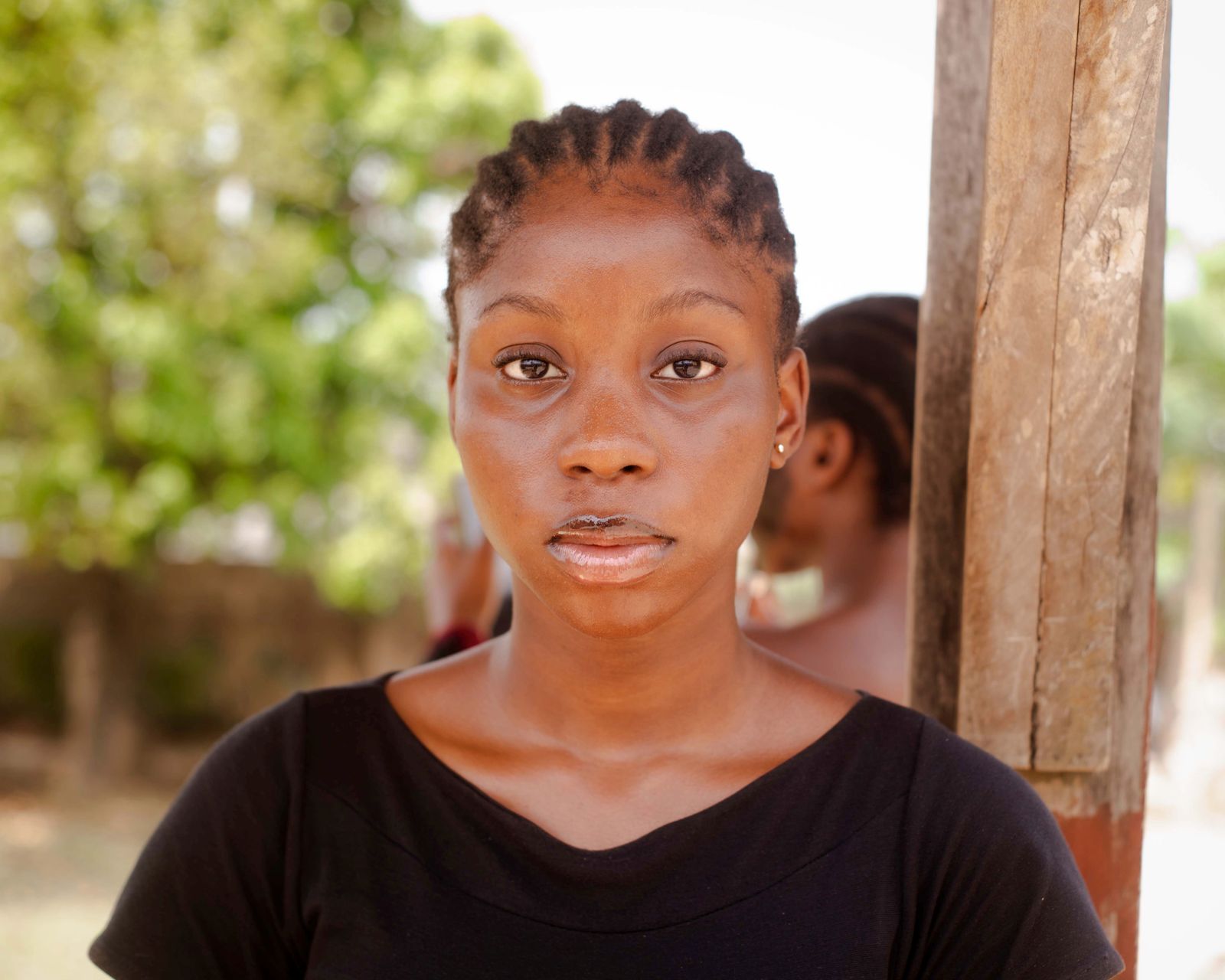 Close-up portrait of a woman wearing a black shirt with cornrow hairstyle, outdoors, under natural light