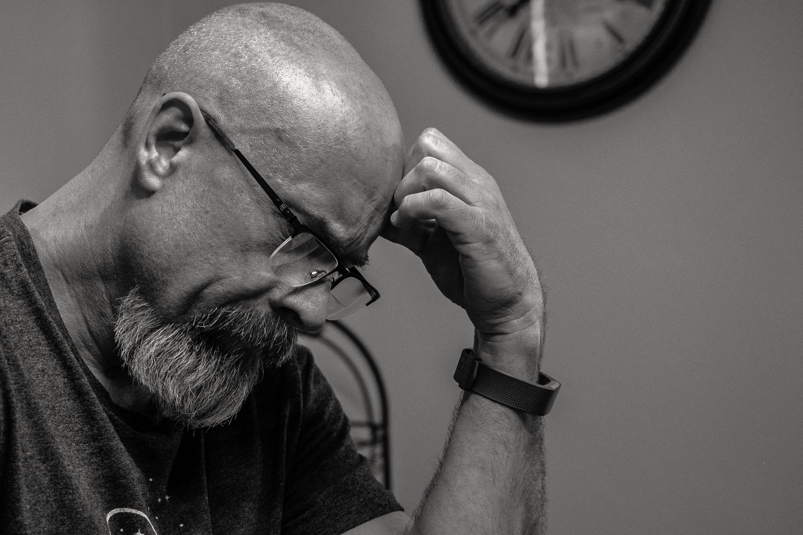 Black and white portrait of a thoughtful bald man indoors, capturing a moment of reflection with a wall clock in the background