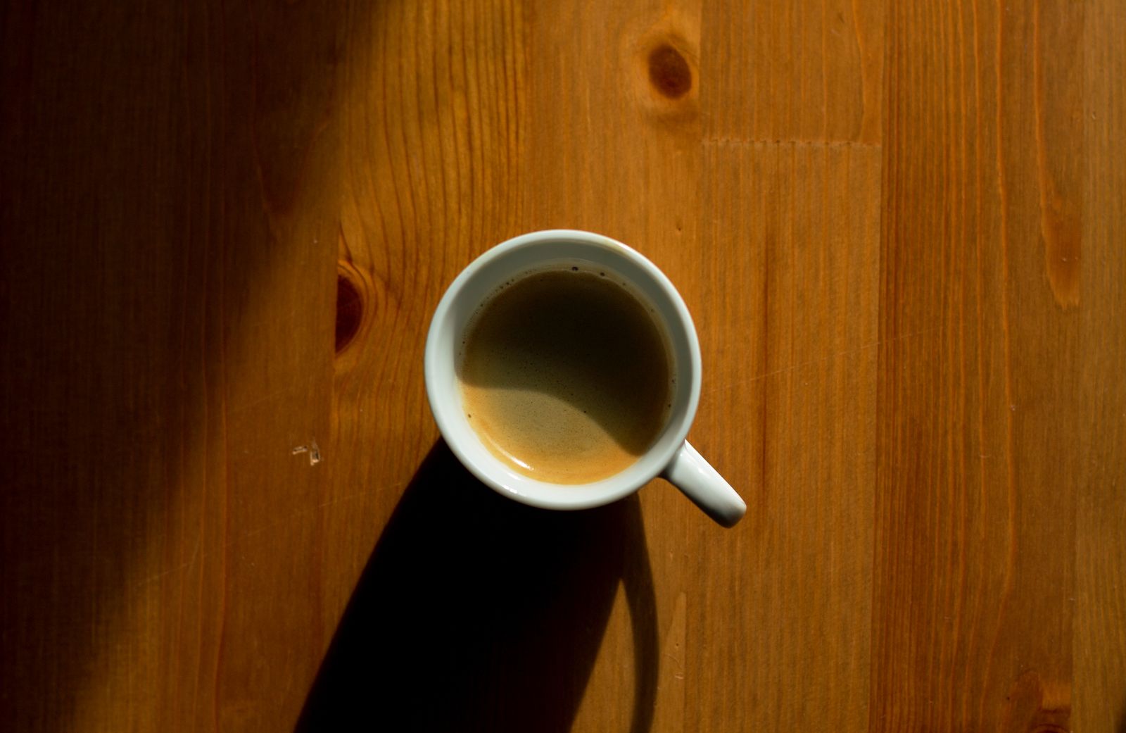 A simple, minimalist approach capturing a cup of coffee casting a shadow on a wooden table