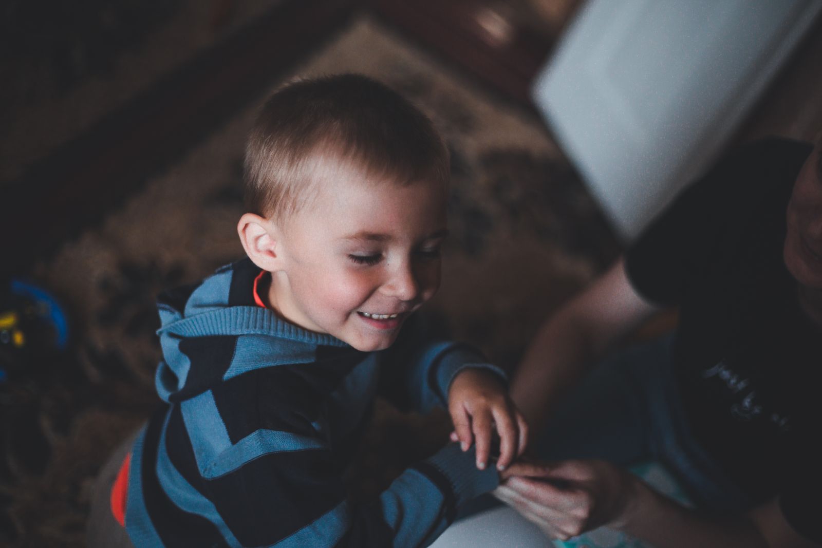 A smiling child in a striped jacket enjoys time indoors with a parent