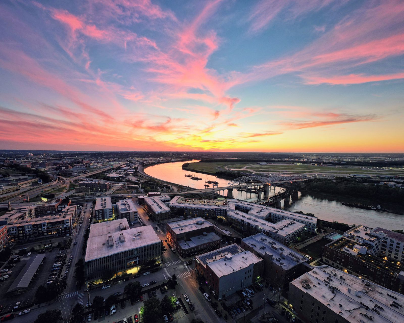 A vibrant sunset over Kansas City's urban landscape and river, highlighting the city's architecture and colorful sky
