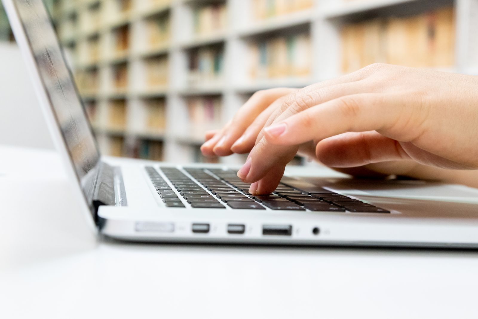Close-up of hands typing on a laptop keyboard in a library setting