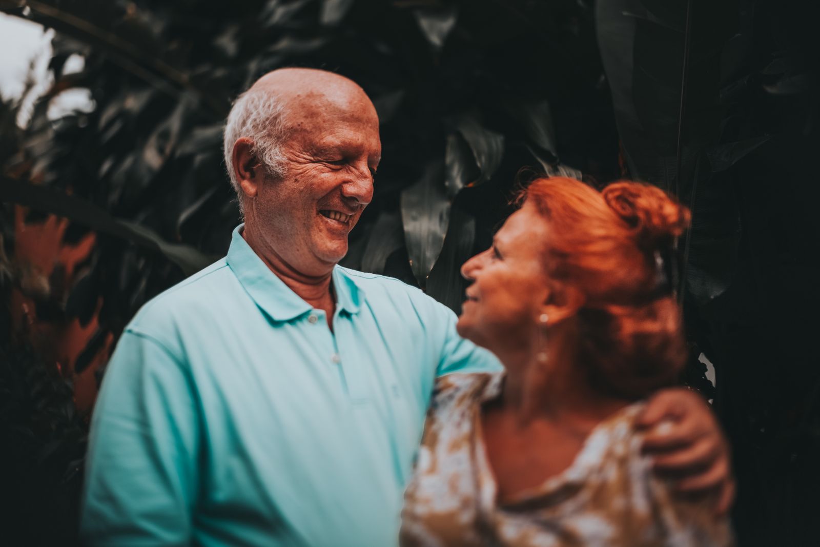 Elderly couple smiling and embracing in lush outdoor setting, capturing love and friendship