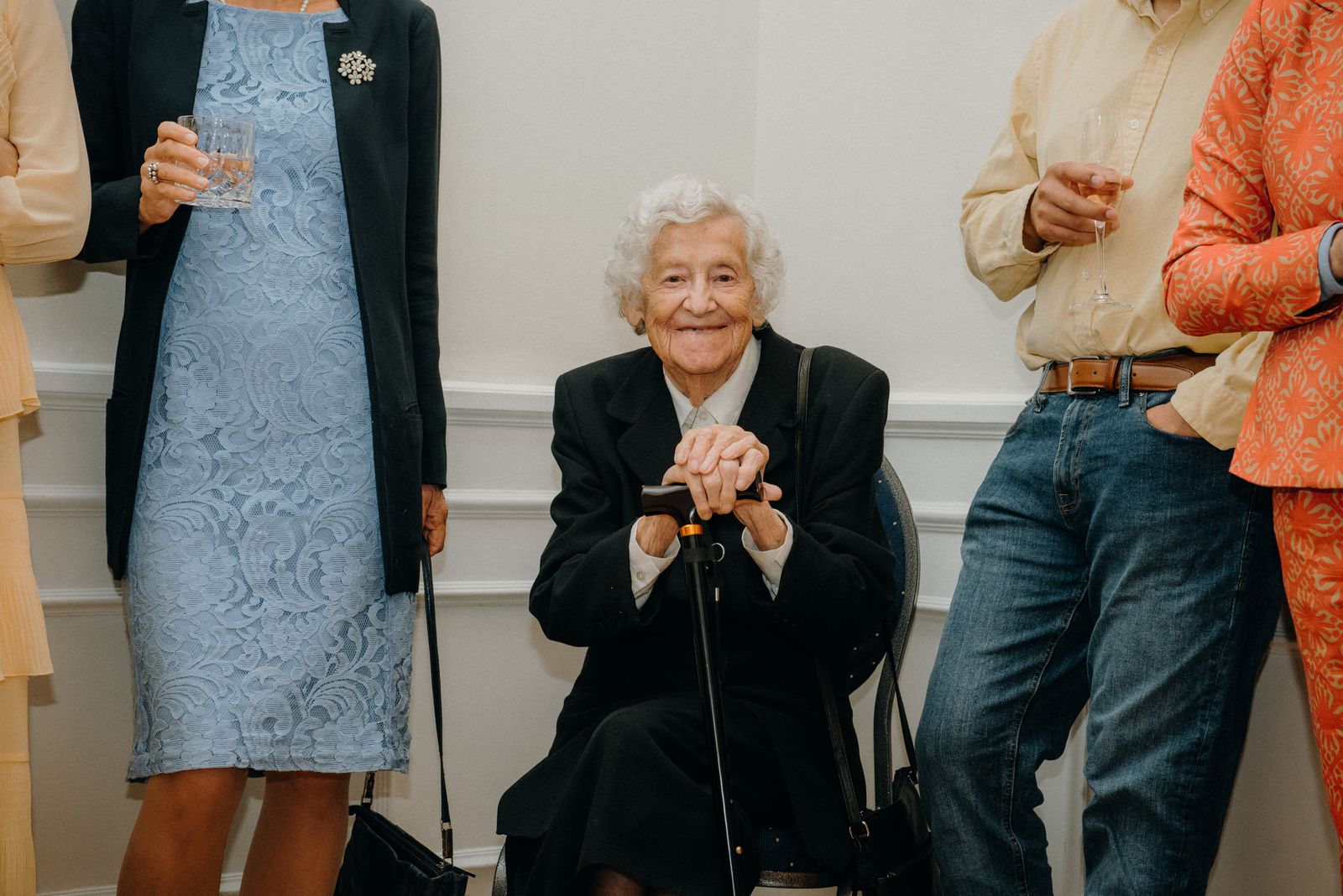 Senior woman smiling at a formal gathering, surrounded by elegantly dressed people