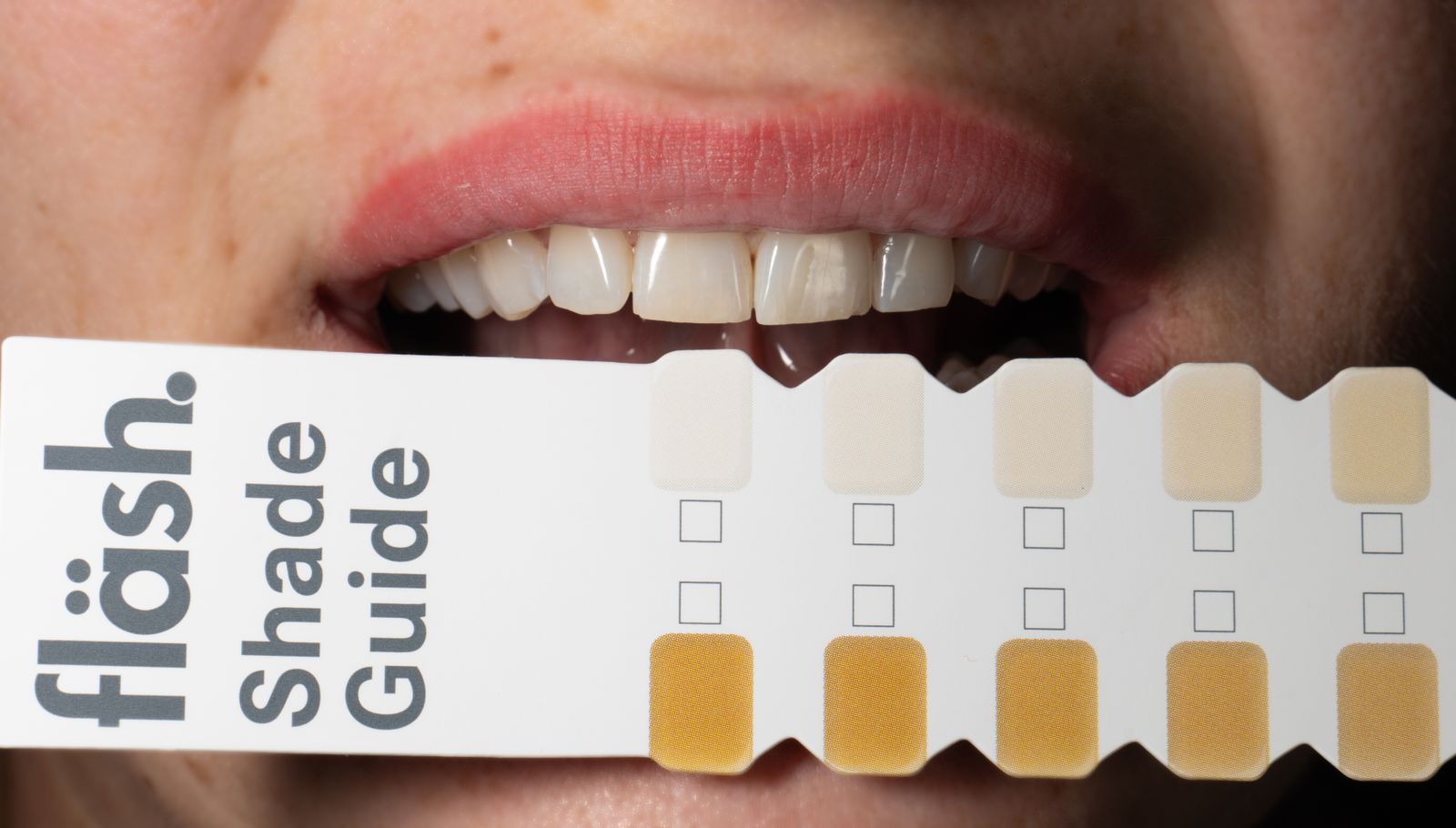 Adult holding a dental shade guide to compare tooth whitening results