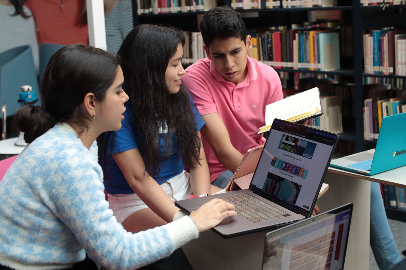 Group of young students studying and discussing in a library setting with books and laptops