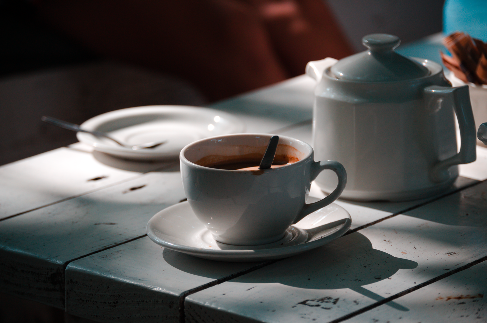 White coffee cup and pot on sun-dappled table, creating a cozy atmosphere