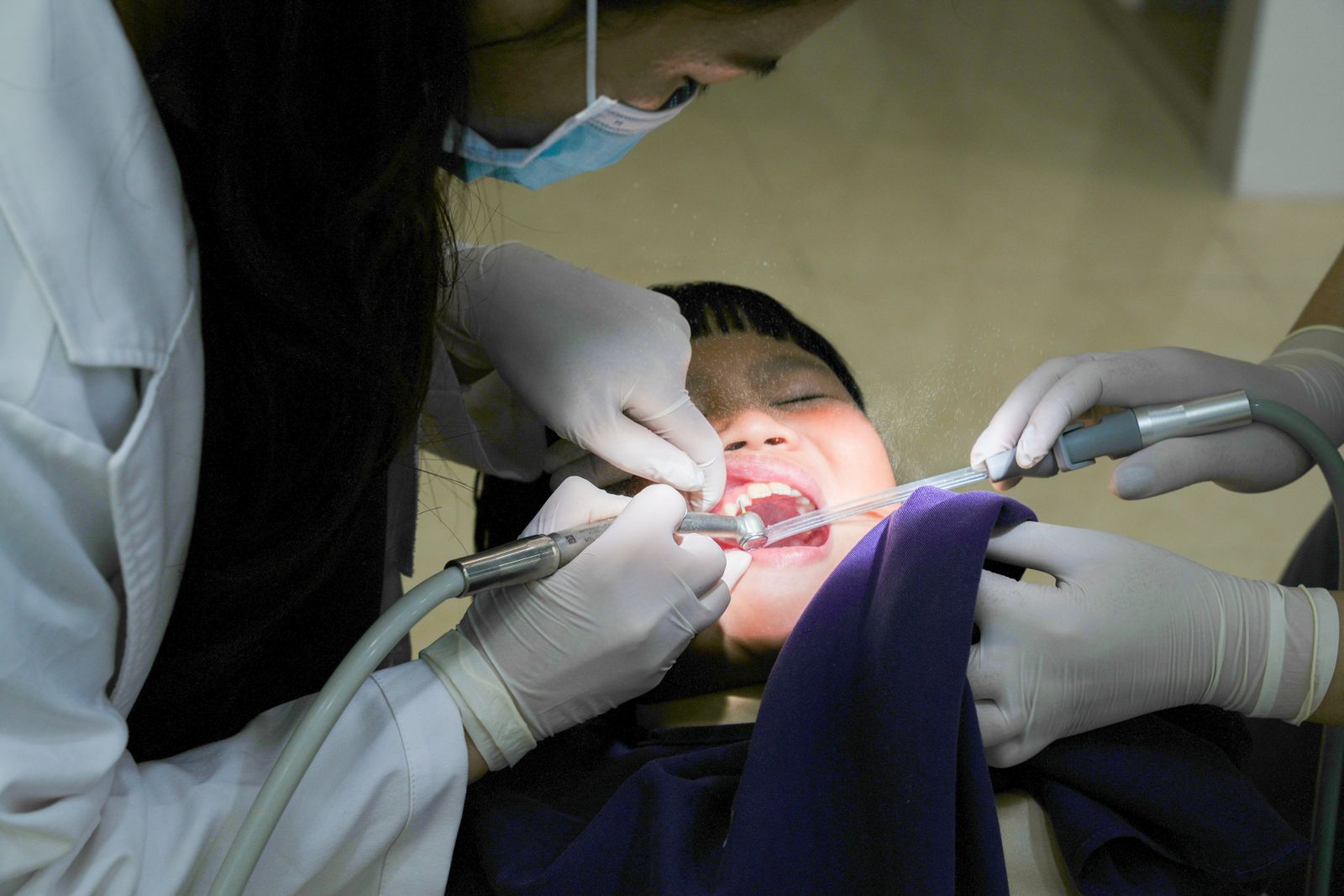 A young child receiving dental treatment from a masked dentist using dental tools indoors