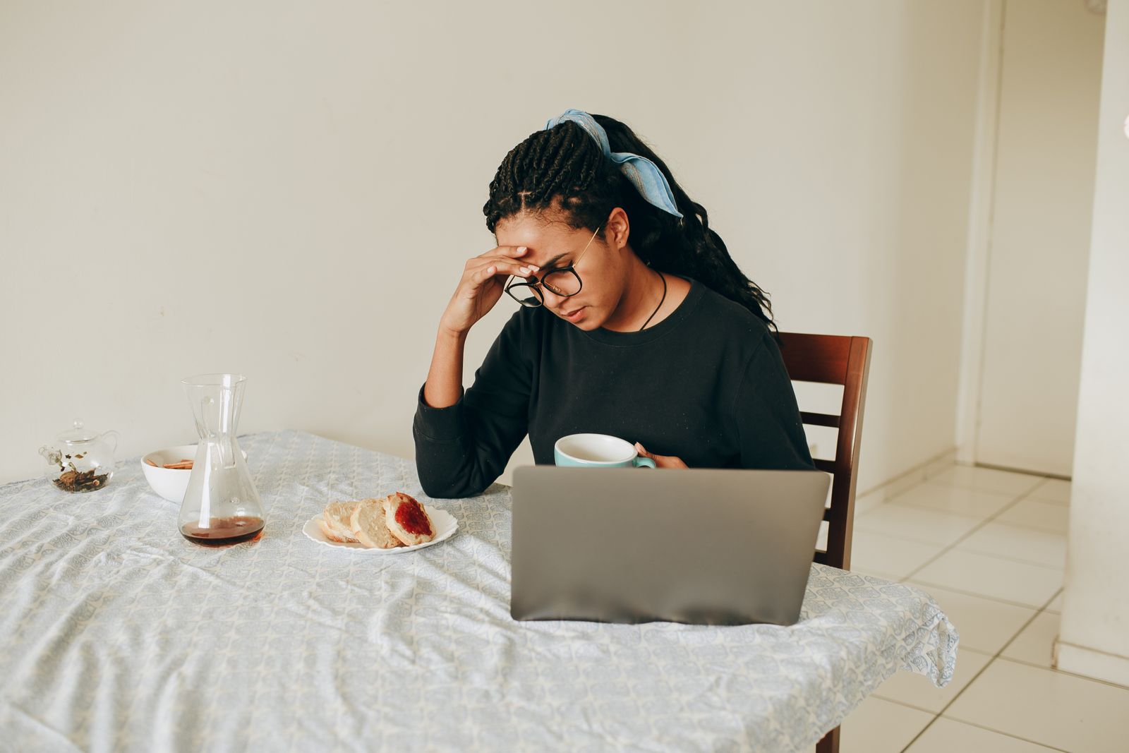 Woman working from home, stressed, drinking coffee, seated at table with laptop