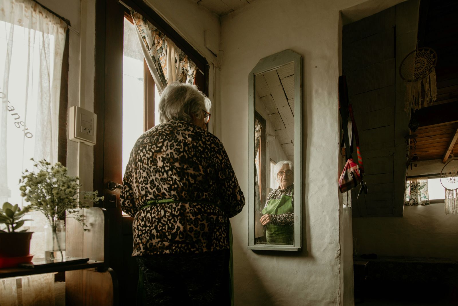 Elderly woman gazes at her reflection in a warm, cozy home setting with decor