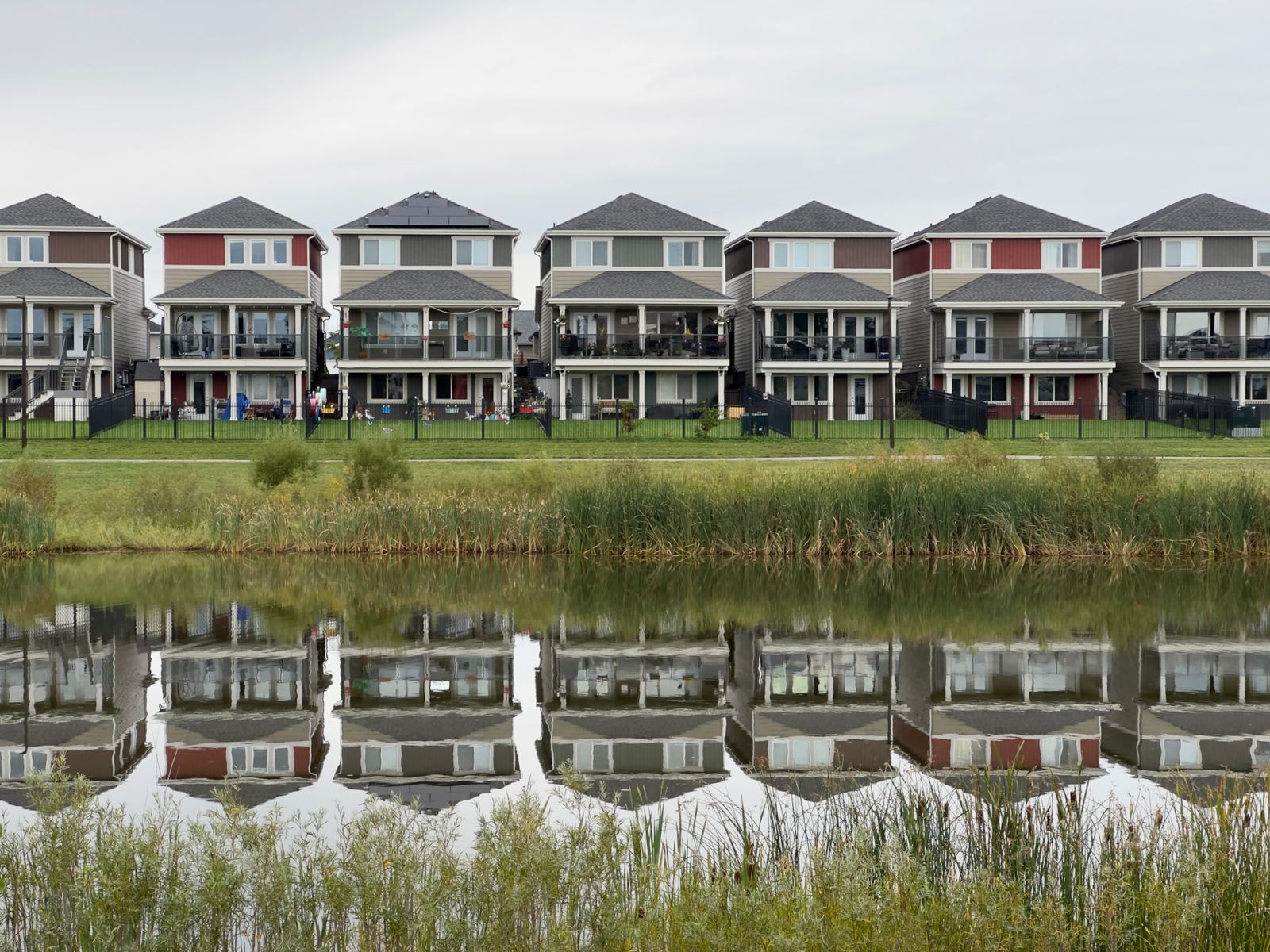 A row of modern houses reflected in a calm pond, showcasing serene suburban architecture