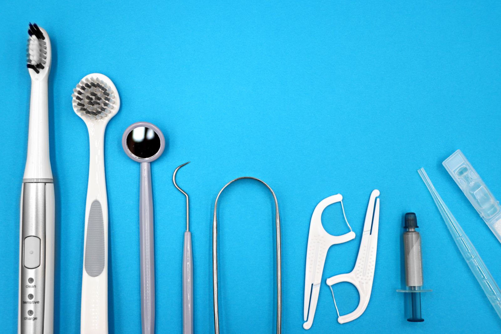 Flat lay of dental care tools including toothbrushes, dental mirror, and floss sticks on blue background