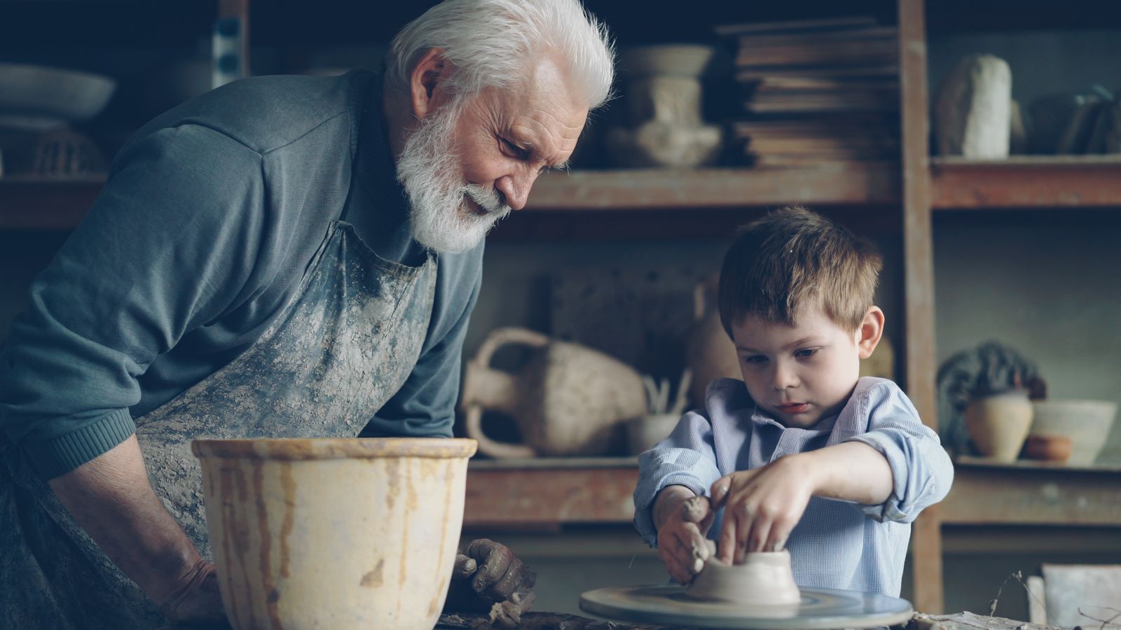 A grandfather teaches his grandson pottery in a creative pottery workshop setting