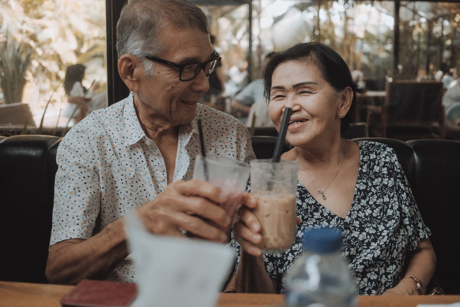 Happy senior couple sharing a moment with iced beverages in a cozy cafe setting
