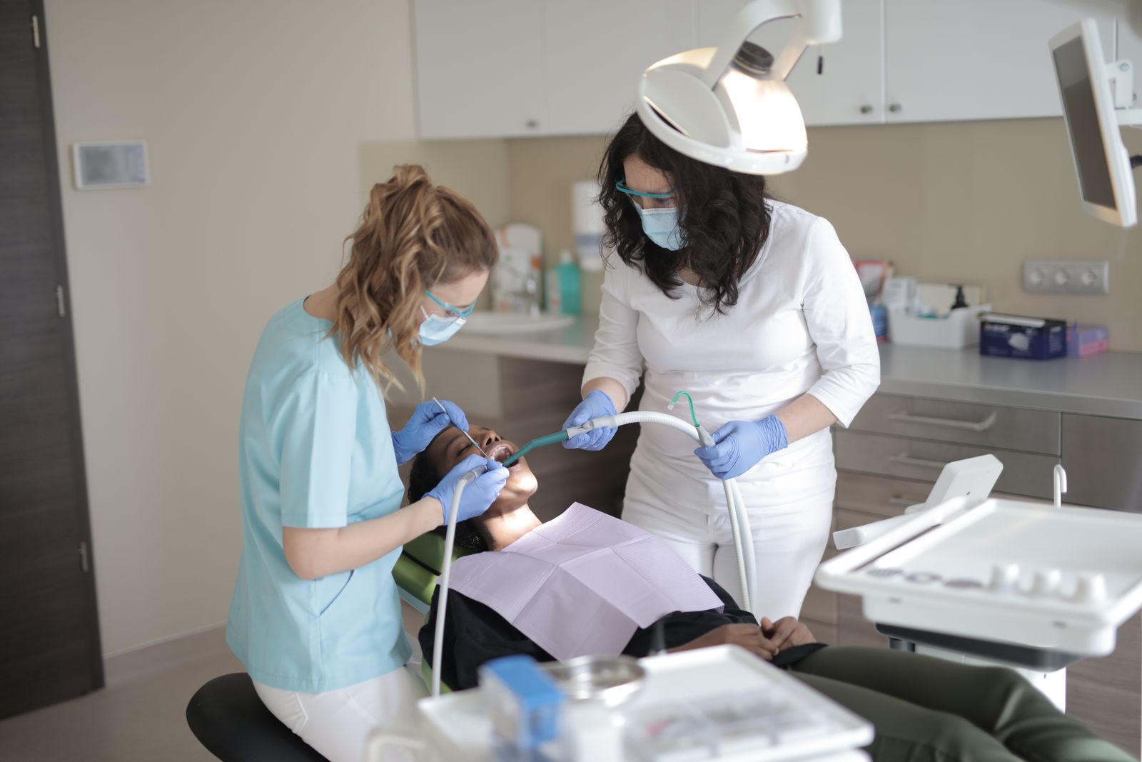 Female dentists in medical masks and latex gloves wearing uniform using medical instruments while treating teeth of female patient