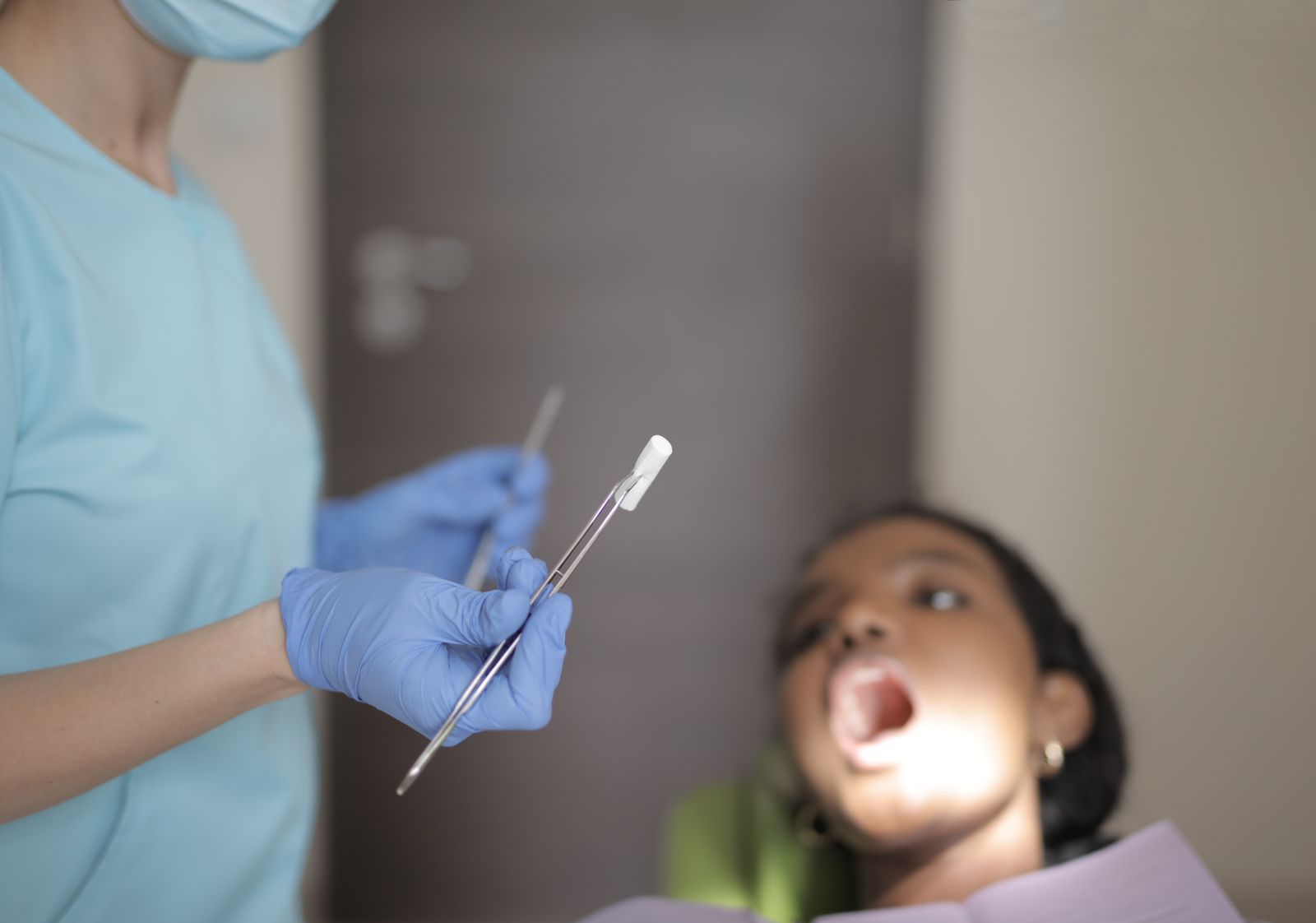 Unrecognizable crop dentist in medical mask and latex gloves wearing blue uniform holding instruments while treating teeth of fema