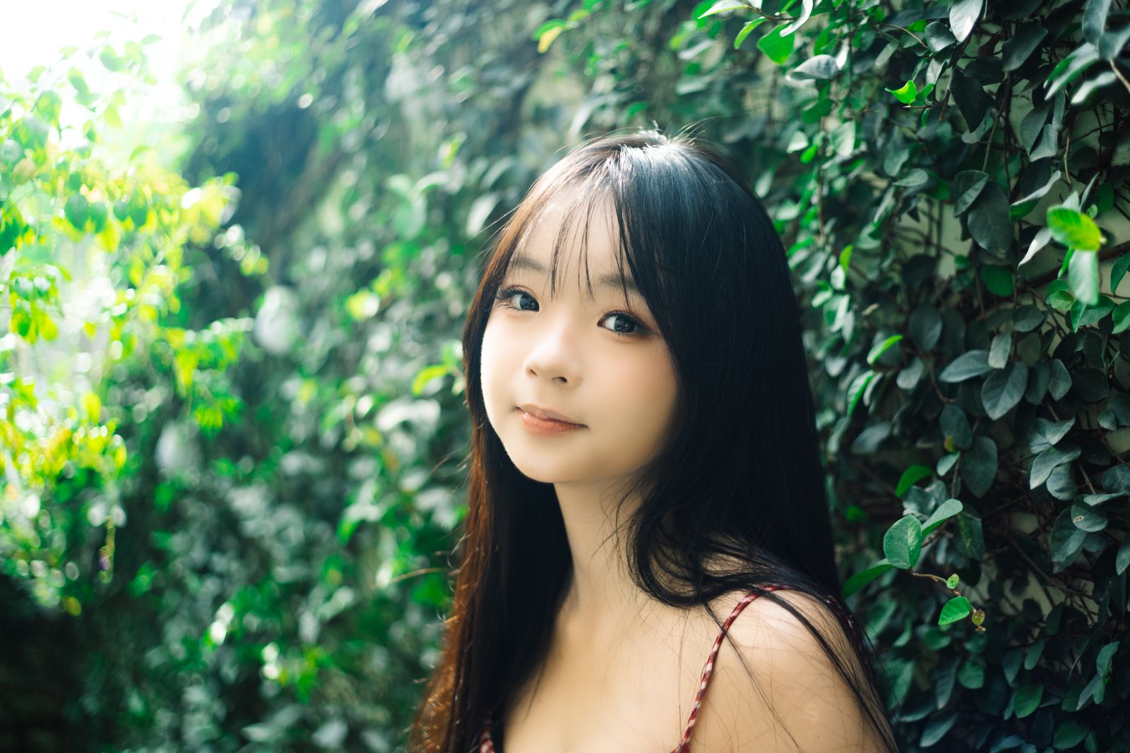 Portrait of a young woman surrounded by lush green foliage creating a tranquil and natural atmosphere