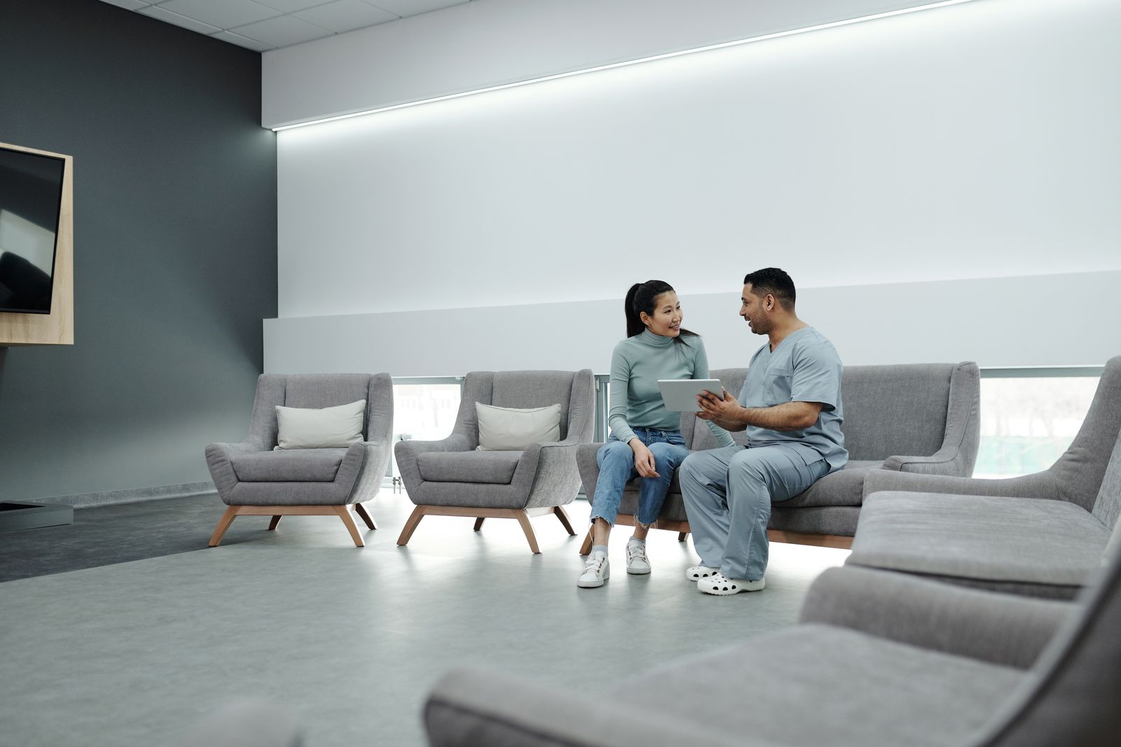 Doctor and patient discussing health in a modern waiting room with digital tablet