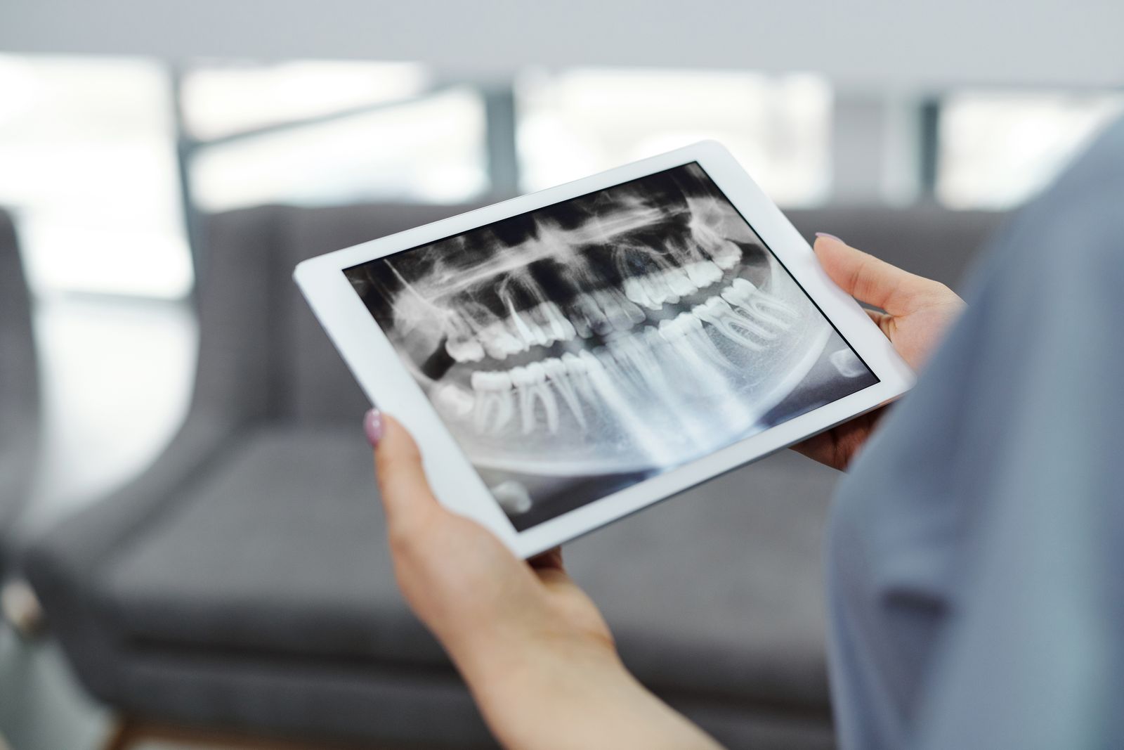 Close-up of hands holding a tablet displaying a dental X-ray indoors