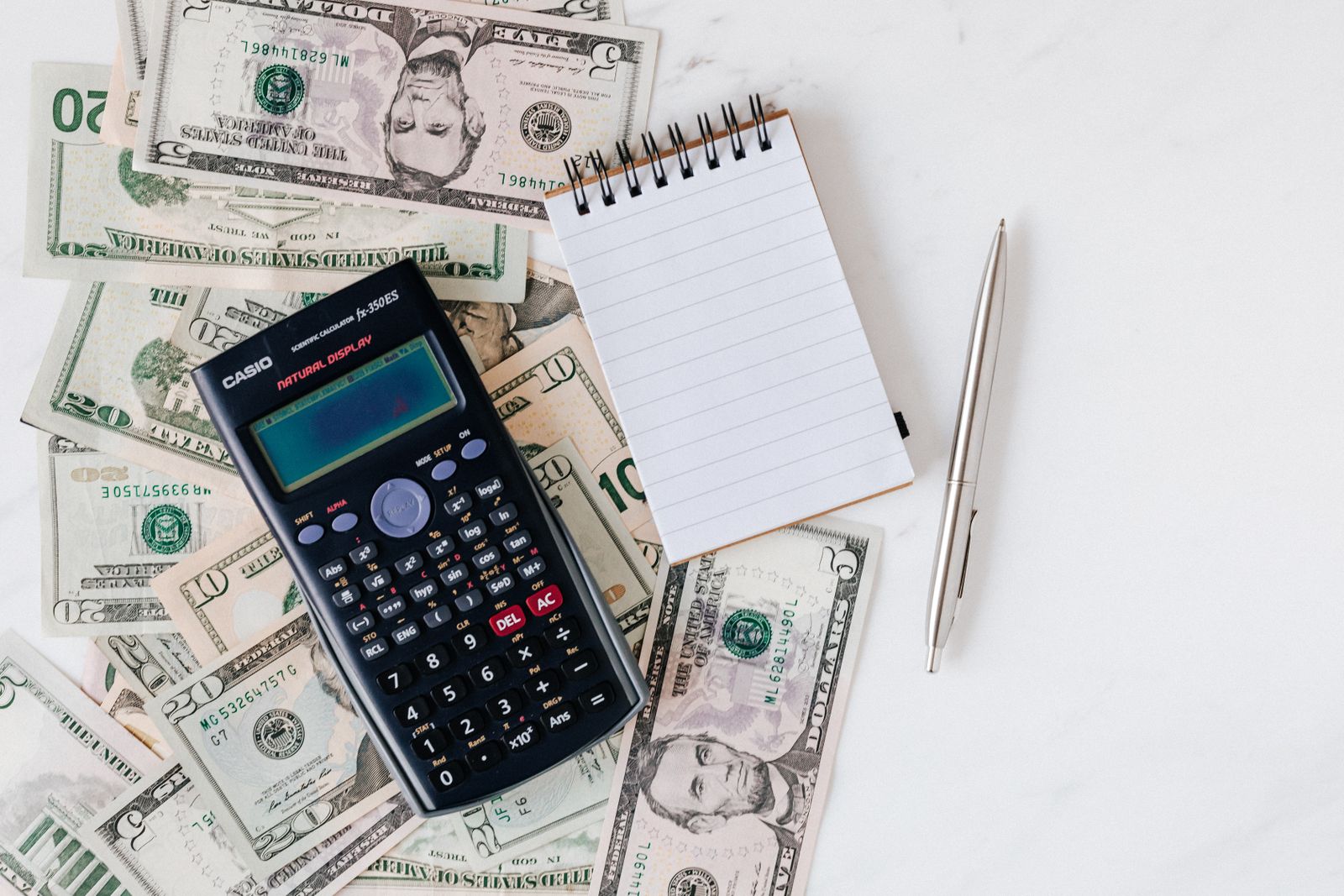 Top view of electronic calculator and notepad placed over United States dollar cash money together with metallic pen for budget pl