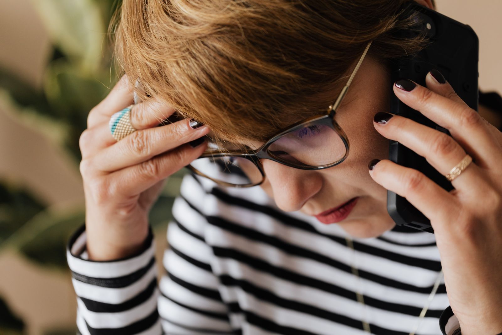 Crop upset adult female manager in eyeglasses feeling sad while having phone discussion during work in office