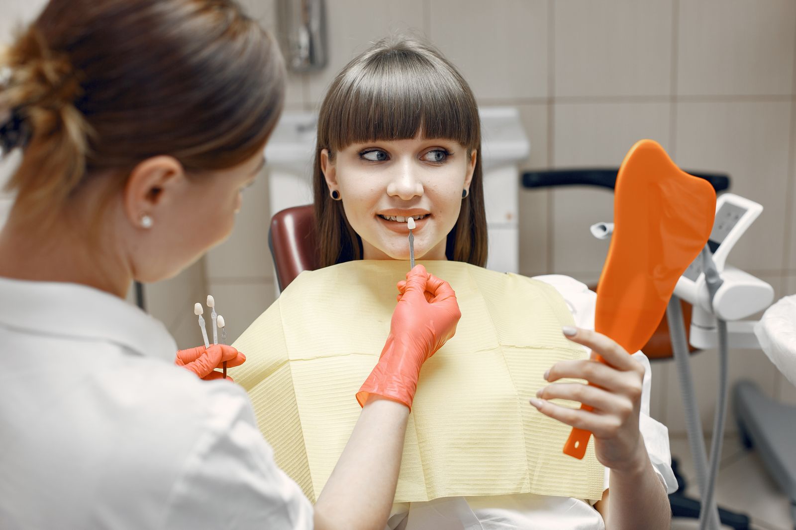 Dentist consults a young woman on veneers using dental tools and mirror in a clinic