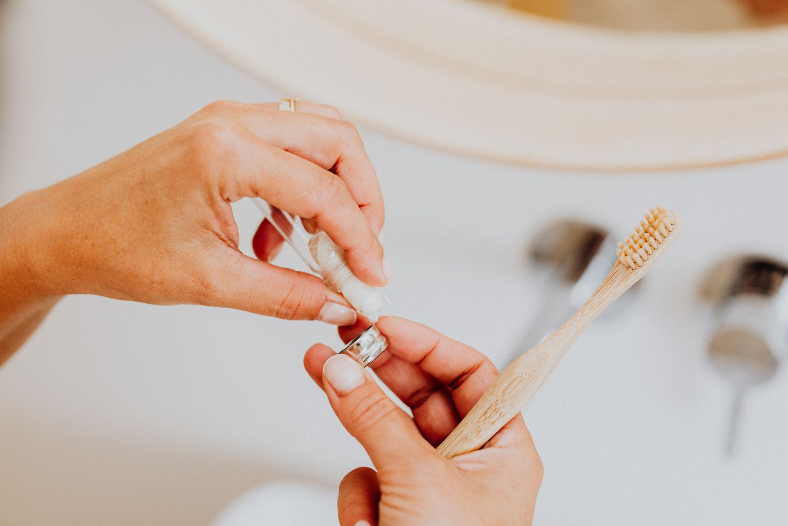 Adult hand applying toothpaste on an eco-friendly toothbrush indoors