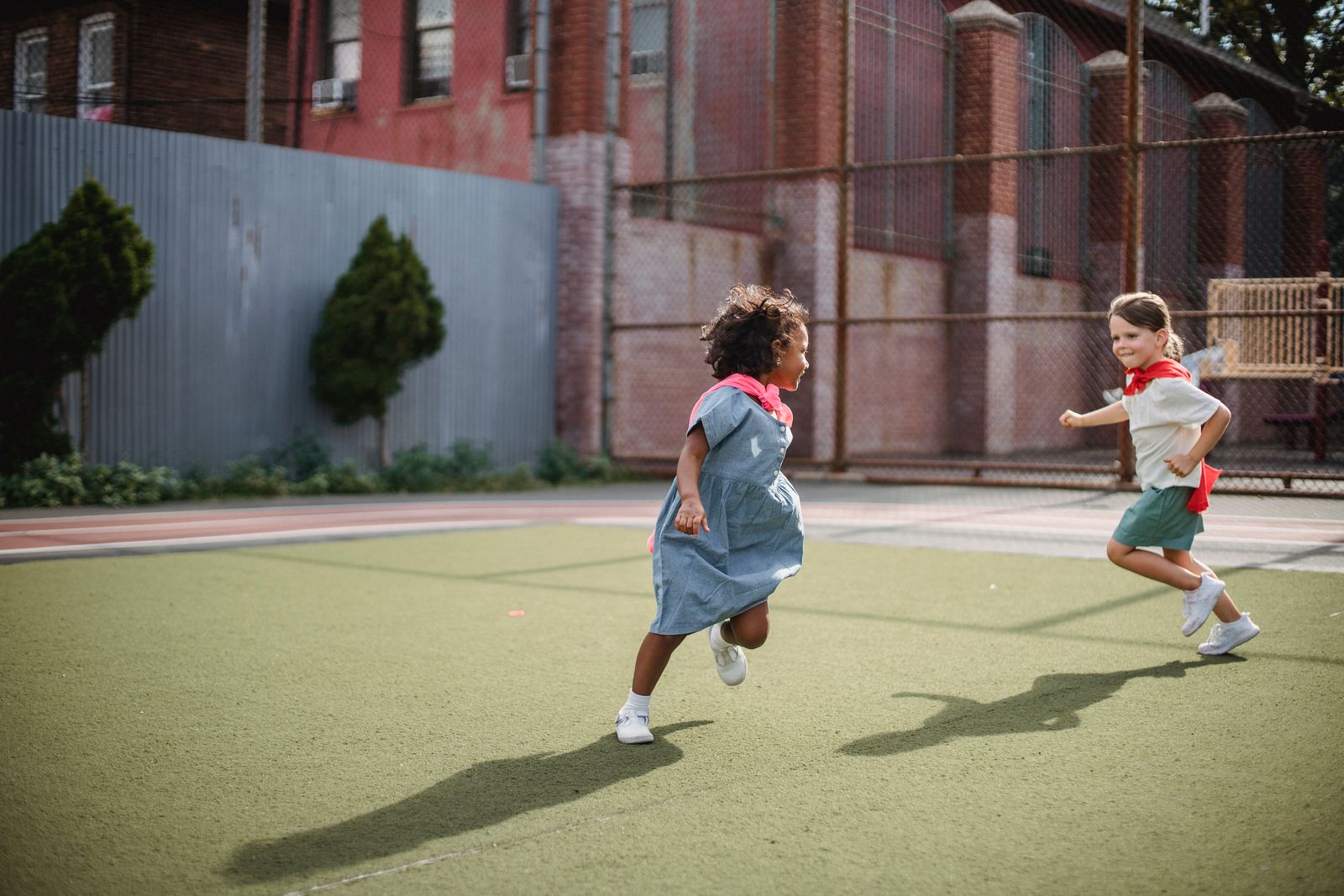 Two children playfully running with capes in an urban playground, enjoying superhero role-play