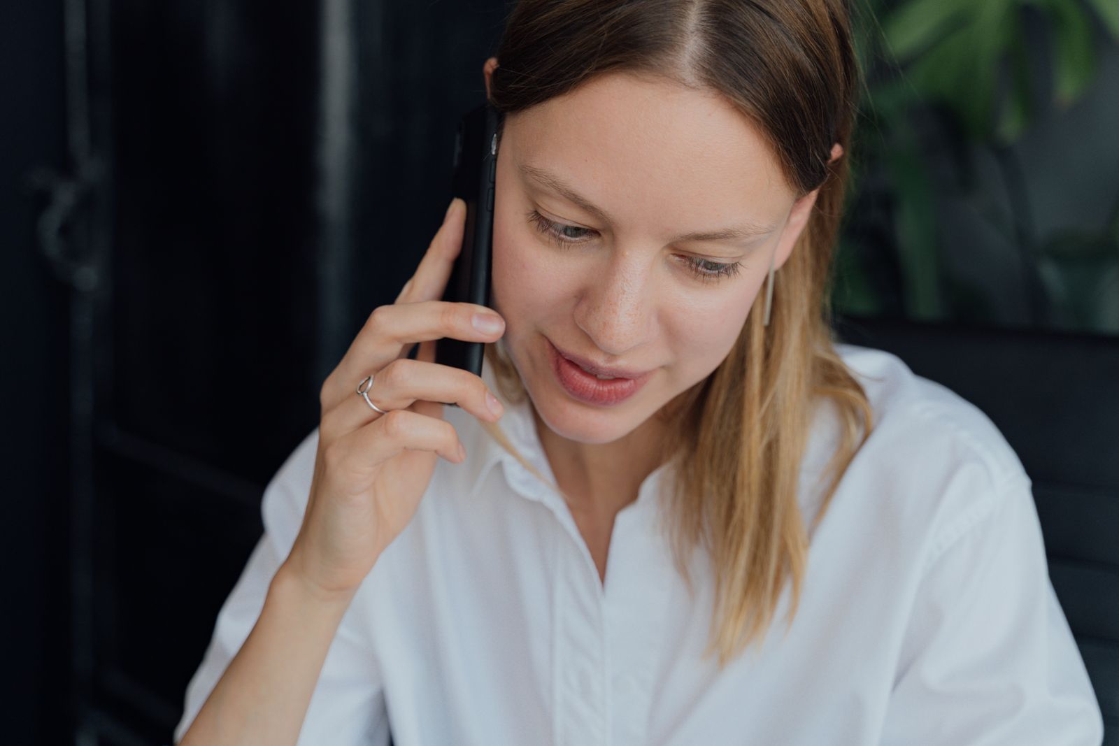 A professional woman in a white shirt making a phone call in an indoor setting, showing communication and business engagement
