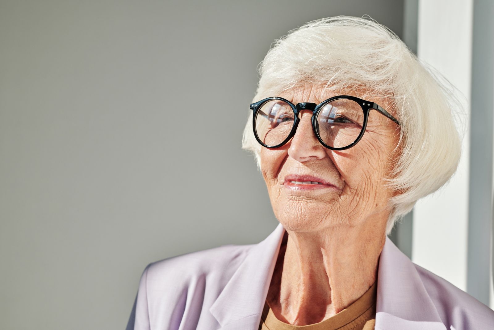 Portrait of a senior woman smiling warmly with eyeglasses and white hair indoors