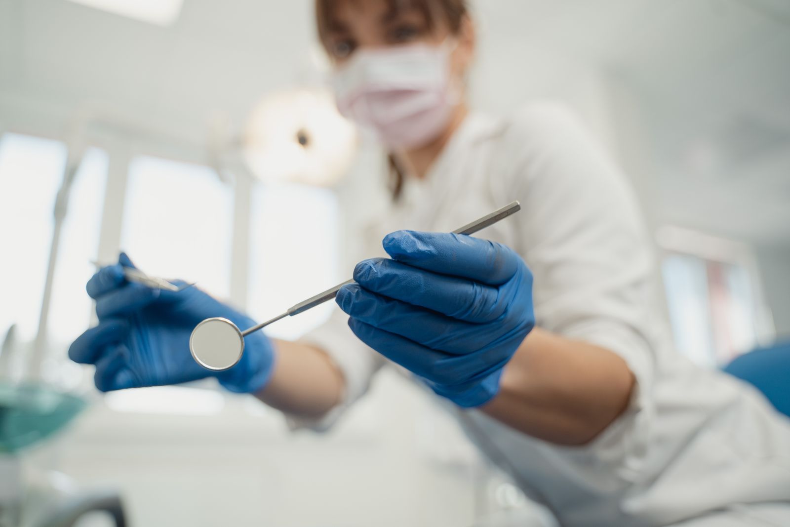A dentist wearing blue gloves holds dental tools in a clinic setting, focused on dental care