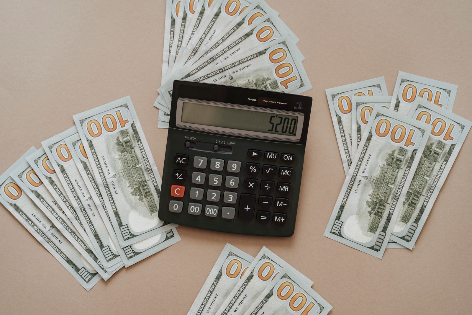 Top view of a calculator showing $5200 surrounded by $100 bills on a tan background