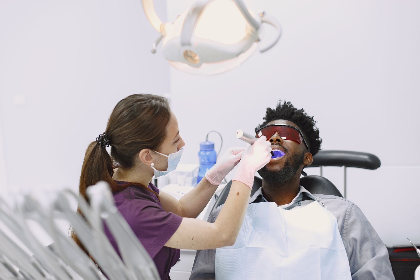 Dentist using curing light on a patient wearing a dental bib during a regular checkup