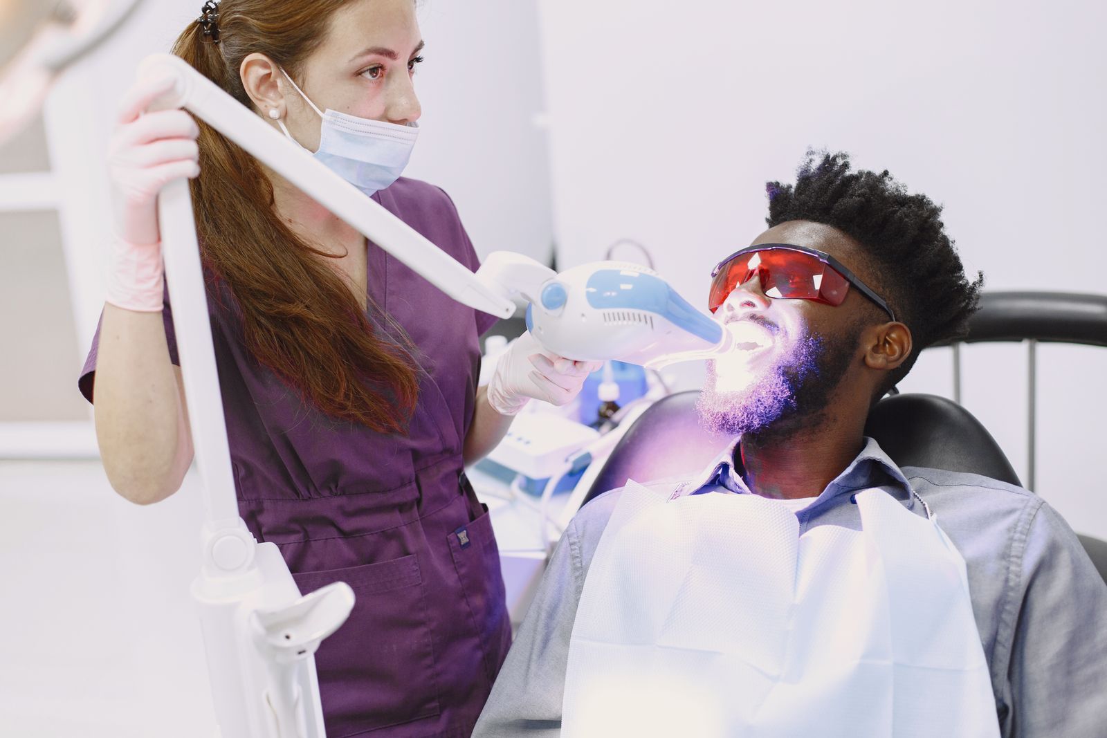 Dentist performing teeth whitening procedure on patient with specialized equipment